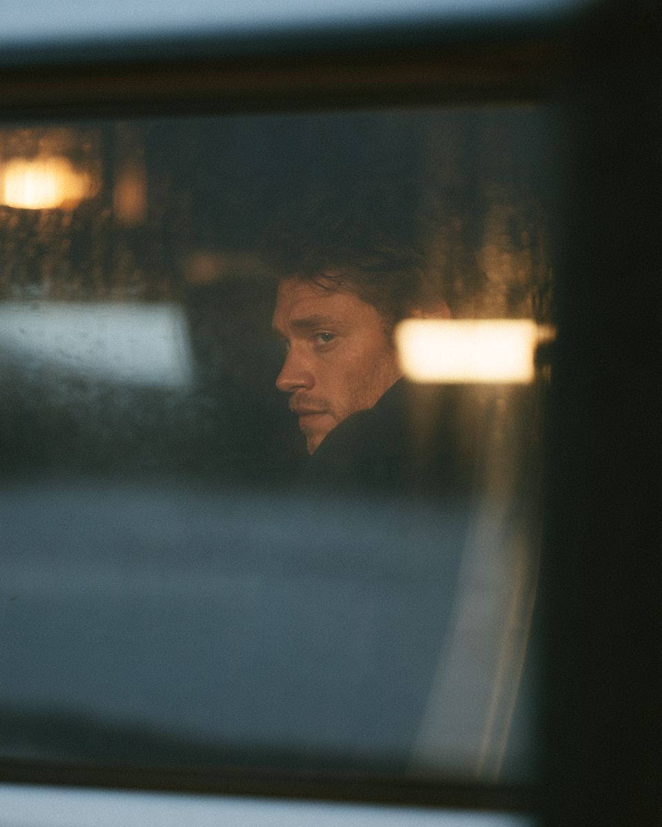 A pilot’s face seen through a rain-streaked window.