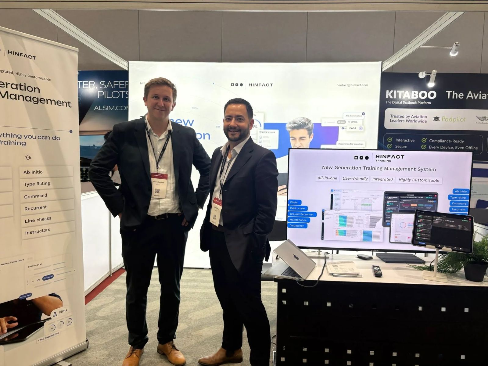 Two members of the Hinfact team on booth 607 at APATS 2026, next to a screen showing Hinfact Training.