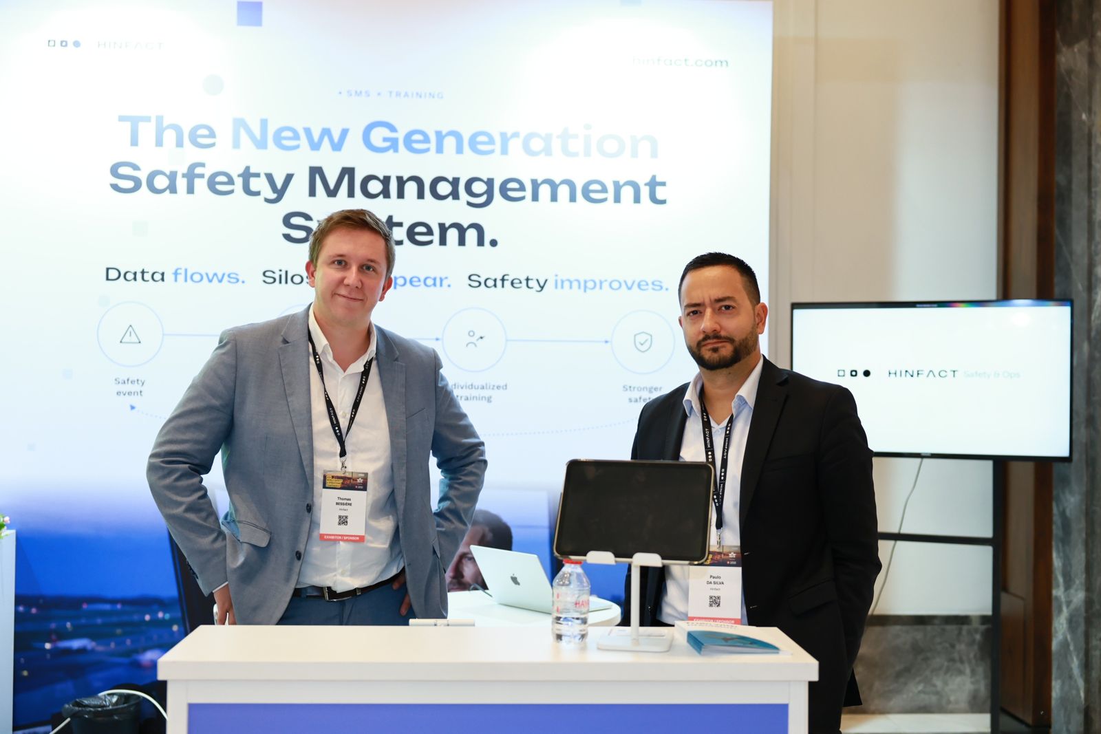 Two members of the Hinfact team on the booth at IATA WSOC 2026, in front of a screen reading "The New Generation Safety Management System".