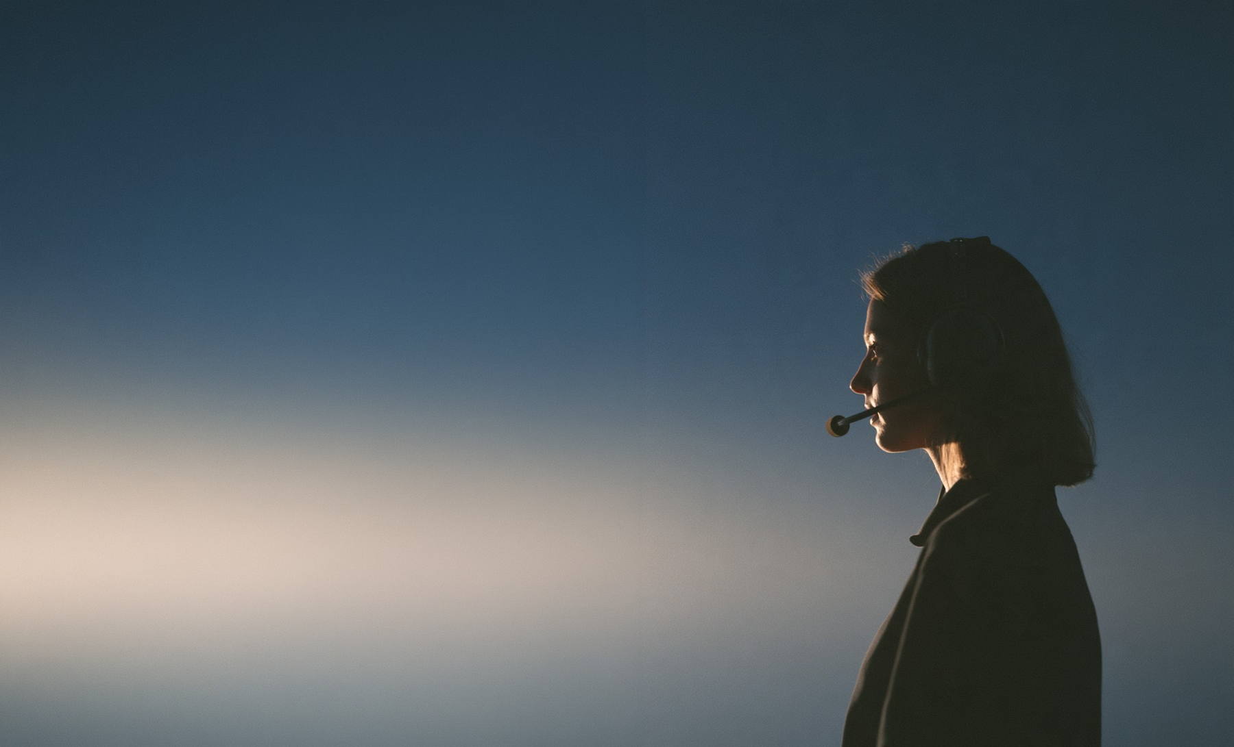 A pilot in silhouette against the dusk sky, headset on.